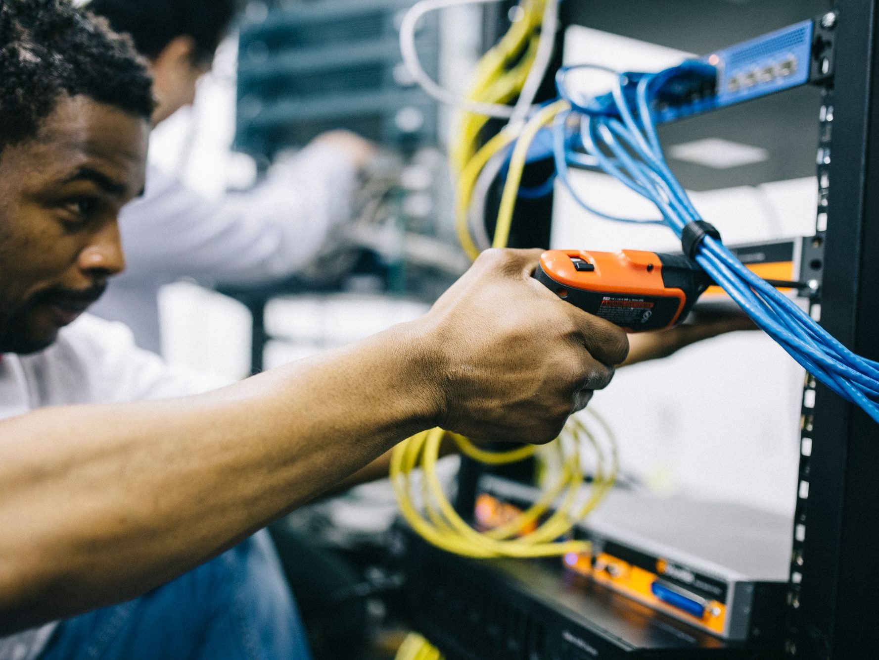 Field technician connecting network cabling inside an equipment rack while a second technician works in the background