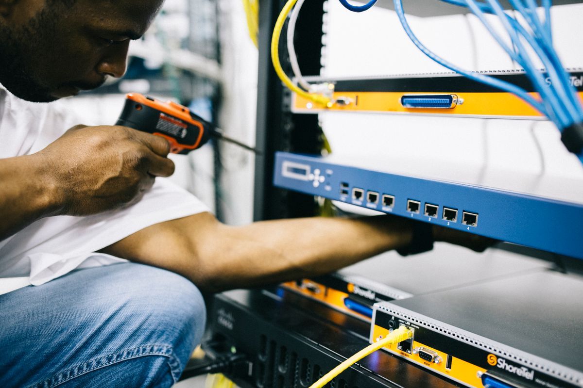 Technician mounting a network switch in a rack alongside patch cabling