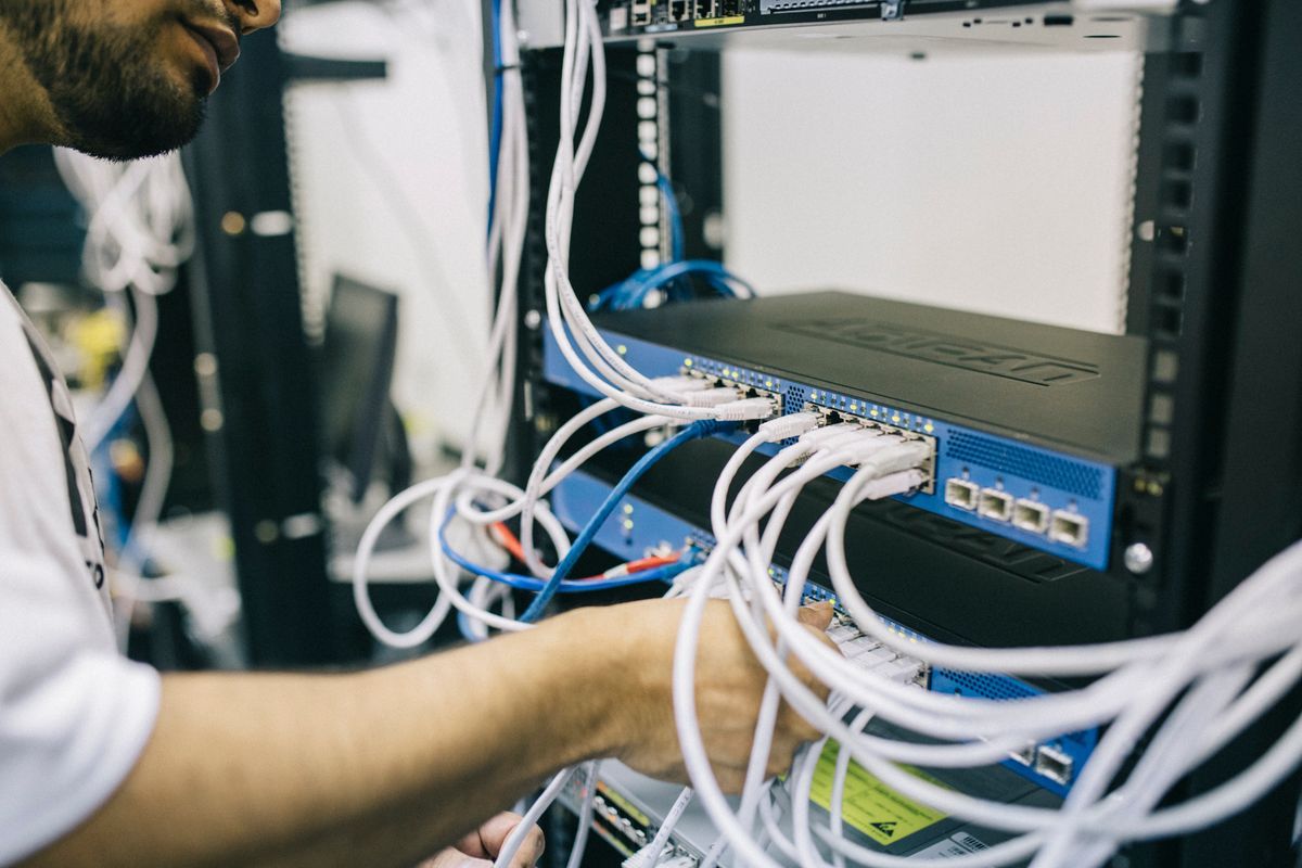 Technician performing cable changes at a network rack under remote direction